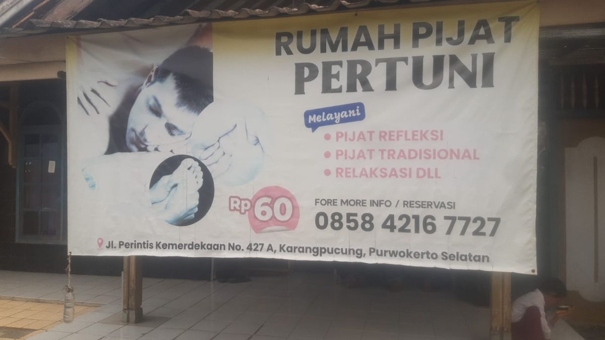 Sebuah spanduk yang dipasang di luar sebuah bangunan. Spanduk tersebut menampilkan gambar seorang pria yang sedang berbaring di atas sebuah meja pijat. Di bagian atas spanduk, terdapat tulisan besar yang berbunyi "RUMAH PIJAT PERTUNI". Di bagian bawah spanduk, terdapat informasi kontak, termasuk nomor telepon dan alamat, serta harga yang ditawarkan, yaitu Rp60.000.